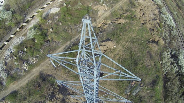 Vârful unui stâlp metalic de înaltă tensiune, fotografiat vertical, cu izolatorii și conductorii