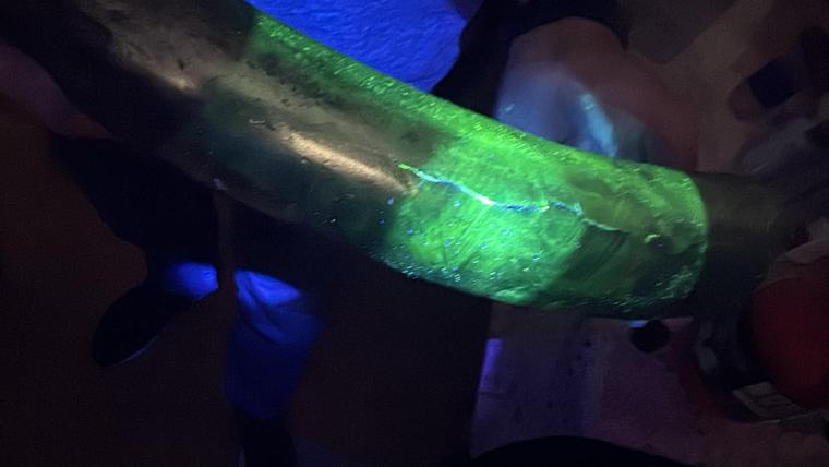 Indicație fluorescentă verde, în formă de linie, pe o piesă metalică luminată cu ultraviolete