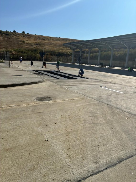 Muncitori montând grătare și semnalizare pe o platformă betonată, lângă un canal tehnic
