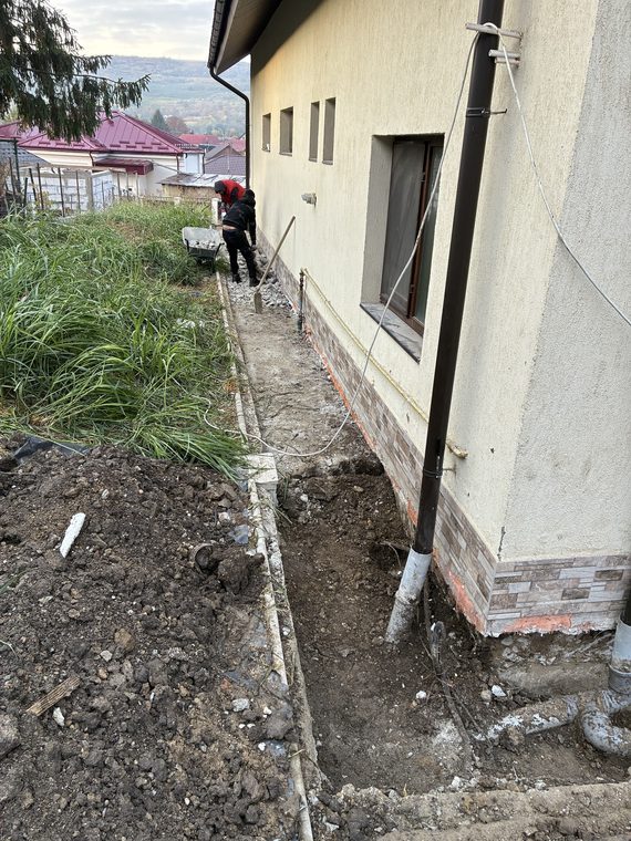 Muncitori care scot trotuarul vechi de-a lungul unei case, pentru remedierea igrasiei